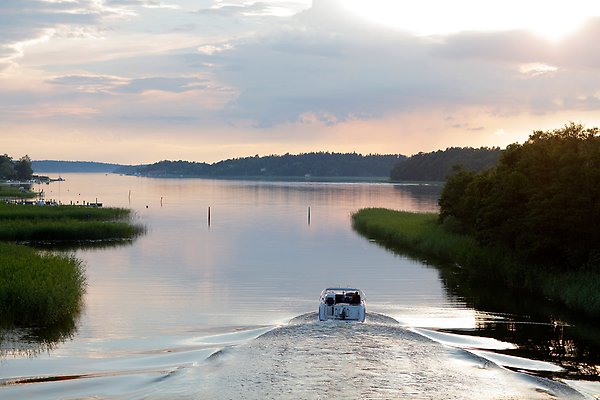 Båt åker på stilla sjö i solnedgång.